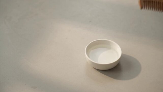 Hand reaching for wooden comb beside white bowl of water on table