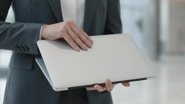 Professional businesswoman standing in corporate office holding laptop computer