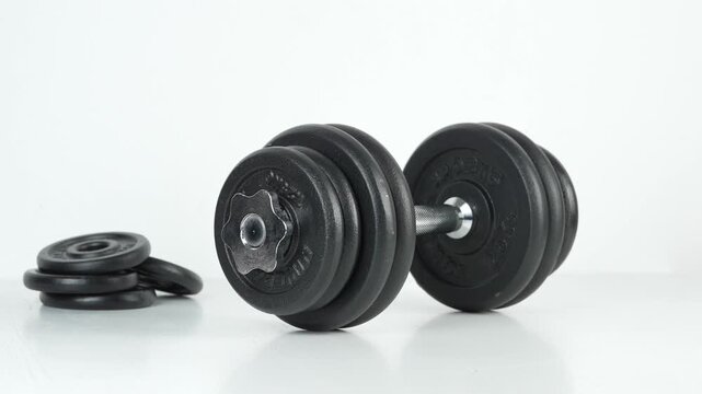 Hand placing a heavy adjustable dumbbell beside weight plates on a clean white background