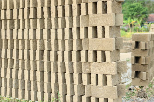 A large stack of unfired clay bricks mixed with straw chaff arranged neatly in rows to dry under the sun