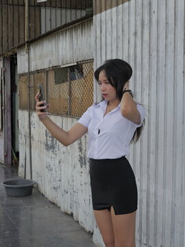 A young Asian woman in a student uniform uses a smartphone to take selfies