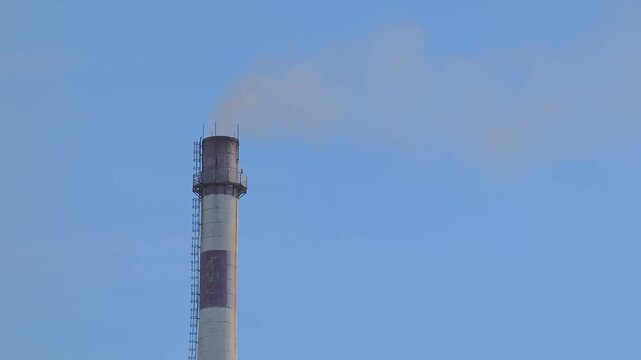 Industrial chimney emitting smoke against a clear blue sky representing environmental pollution and energy production with potential impact on climate change
