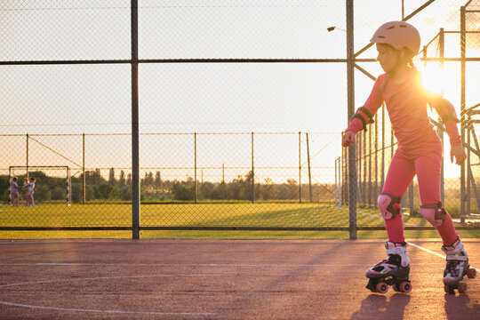 Child roller skating on a sunny evening at an outdoor sports court