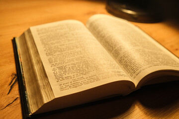 Fototapeta premium Book opened on a wooden table illuminated by a lamp