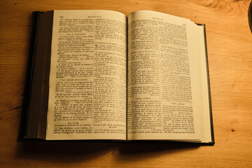 Fototapeta premium Open book on wooden table with text in Spanish and warm light illuminating the pages