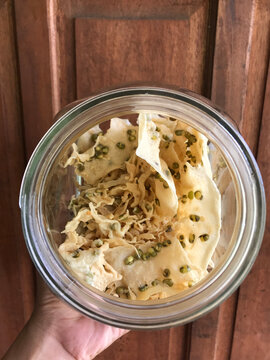 Top view of Indonesian Rempeyek Kacang Hijau (mung bean crackers) inside a clear glass jar against a wooden background