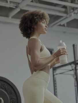 Young athletic woman with an afro hairstyle drinking a protein supplement from a shaker in a gym