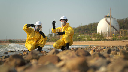 Fototapeta premium Scientists in yellow suits are collecting water samples from the coastline, flowing away from an oil refinery,