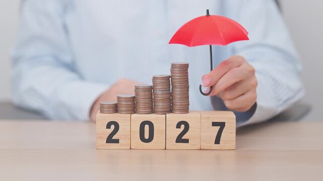 Happy New Year 2027 with hand holding red umbrella and money stack growing. Insurance, protection, safety and New year holiday Concepts