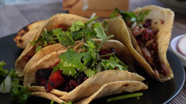 Tacos with fresh cilantro and lime, arranged on a dark plate. Ideal for restaurant advertisements, food blogs, or cultural events.