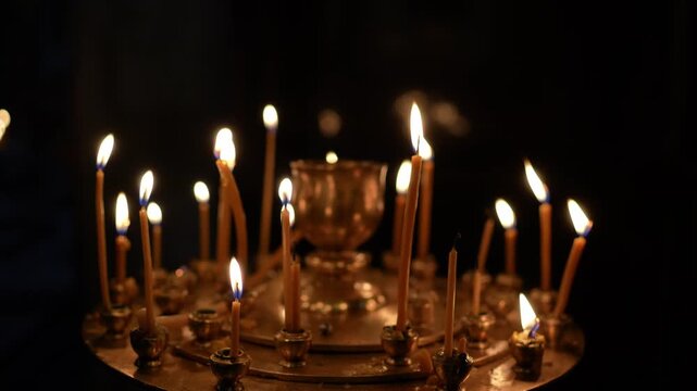 Many thin beeswax candles burning on a circular metal stand inside a dark church interior