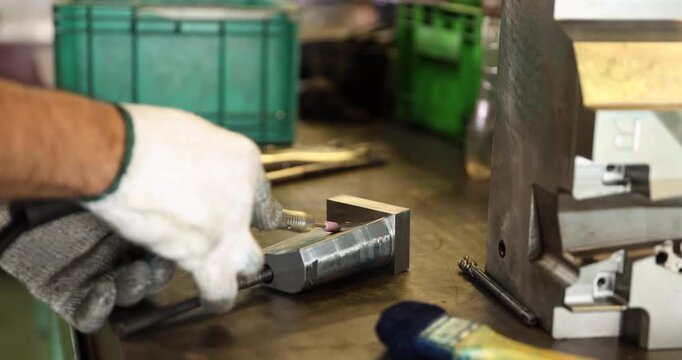 Close-up of gloved hands using a small rotary grinding tool to finish a metal component on a workbench. The scene highlights precision surface finishing, mold tooling
