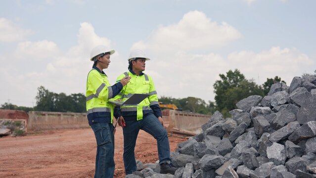 Asian male and female engineers checking riprap stone pile for erosion control at bridge site. Civil infrastructure development, soil protection and engineering teamwork concept.