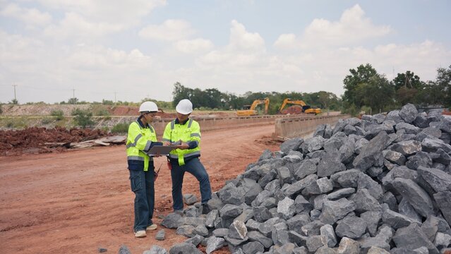 Asian male and female engineers checking riprap stone pile for erosion control at bridge site. Civil infrastructure development, soil protection and engineering teamwork concept.