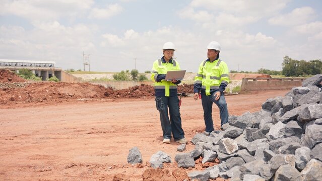 Asian male and female engineers checking riprap stone pile for erosion control at bridge site. Civil infrastructure development, soil protection and engineering teamwork concept.
