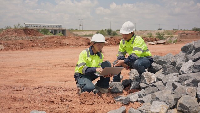 Asian male and female engineers checking riprap stone pile for erosion control at bridge site. Civil infrastructure development, soil protection and engineering teamwork concept.
