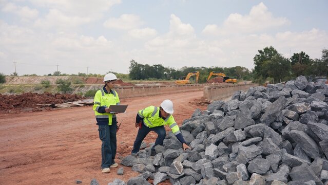 Asian male and female engineers checking riprap stone pile for erosion control at bridge site. Civil infrastructure development, soil protection and engineering teamwork concept.