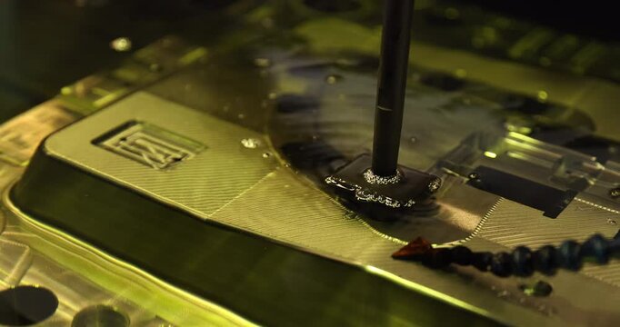 Close-up of industrial mold manufacturing, showing a vertical tool positioned over a metal workpiece with fluid and bubbles around the working area.