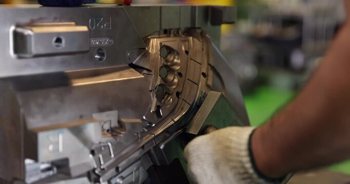 Close-up of gloved hands positioning a metal component during mold assembly in an industrial workshop. Detailed tooling and machined surfaces highlight skilled manual work and precision manufacturing.