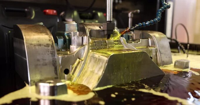 Close-up of a metal mold being machined as fluid flows through a flexible nozzle onto the working area. Detailed industrial tooling illustrates precision manufacturing