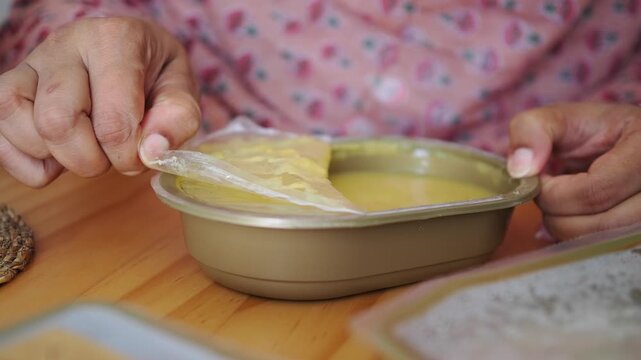 Person Peeling Plastic Film Off Prepackaged Food Container
