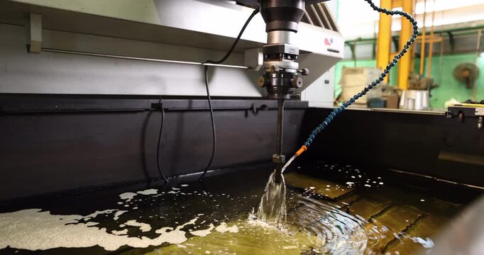 Close-up of a metal mold being machined as fluid flows through a flexible nozzle onto the working area. Detailed industrial tooling illustrates precision manufacturing