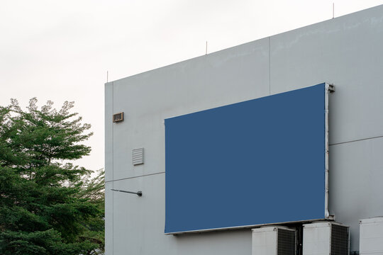 Large blank blue billboard mounted on the exterior wall of a modern commercial building, suitable for advertisement mockup.