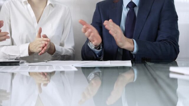 Unrecognizable business professionals applauding and celebrating achievements at glass table after successful meeting. Business people concept, close up view