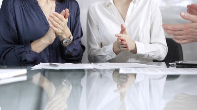 Unrecognizable business professionals applauding and celebrating achievements at glass table after successful meeting and contract signing. Business people concept, close up view