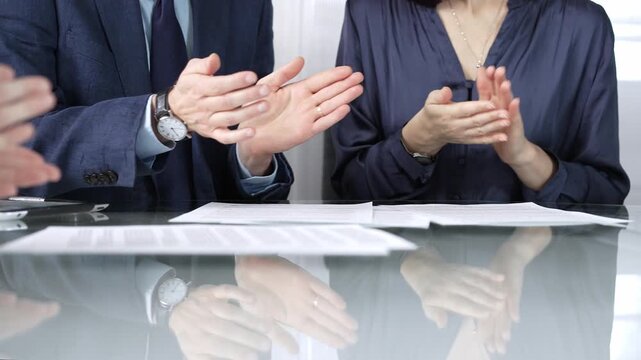 Unrecognizable business professionals applauding and celebrating achievements at glass table after successful meeting and contract signing. Business people concept, close up view