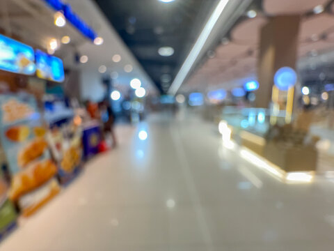 Blurred image of people walking down a wide, well-lit corridor in a modern shopping mall or large retail center, with colorful bokeh lights.