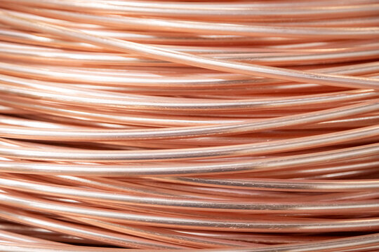 Close-up of coiled copper wires, showcasing their shiny surface and intricate overlapping pattern, captured in warm lighting.