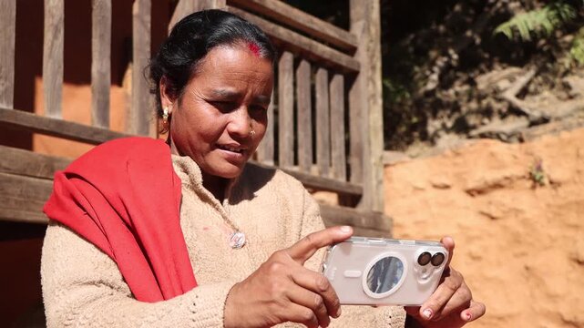 A rural village woman is holding and viewing a modern smartphone outdoors in the sunlight.