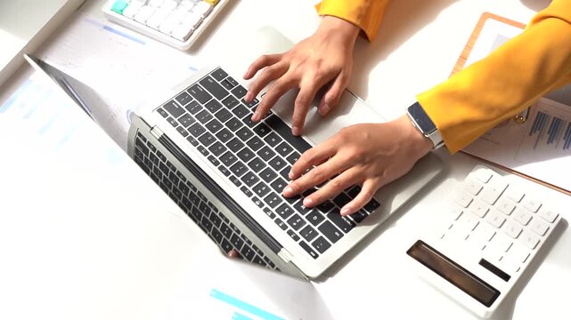 Hands Typing on Laptop: A close-up of hands actively typing on a modern laptop keyboard, surrounded by financial documents and calculator, suggesting a focused work session.