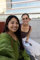 Fototapeta premium Two smiling friends taking a selfie together, sharing a joyful moment during their urban travel adventure and experiencing the vibrancy of the city as tourists