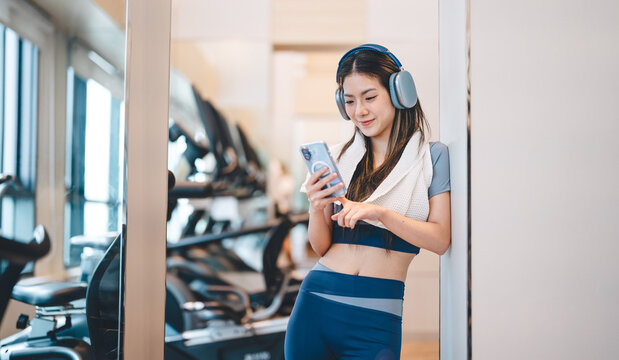 Asian woman, wear sportswear with headphone, cool down exercise using smartphone training app at indoor gym post workout