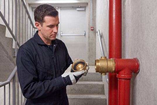 Worker Examining Brass Fire Hose Coupling in Stairwell