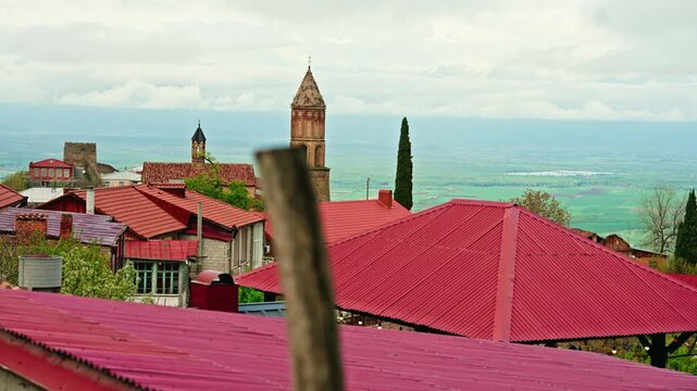 Layer upon layer of red tiled roofs, balconies and a brick bell tower fill the frame in this telephoto view of Sighnaghi.