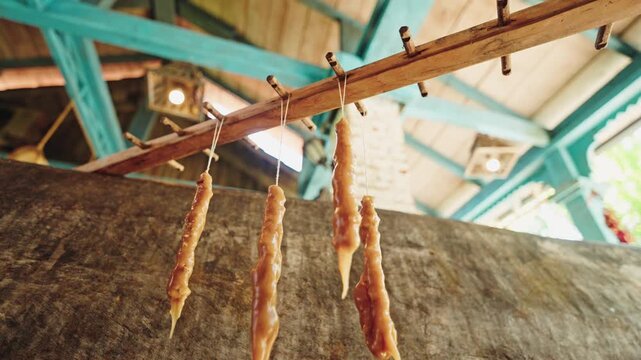 A hand ties freshly dipped churchkhela onto a wooden rod to dry beneath the turquoise beams of a Georgian winery kitchen.