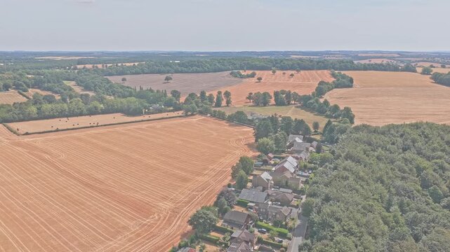 Newmillerdam Country Park farmland near Wakefield, West Yorkshire, England, shows harvested cereal fields with parallel combine lines, woodland and rural homes, drone forward flyover.