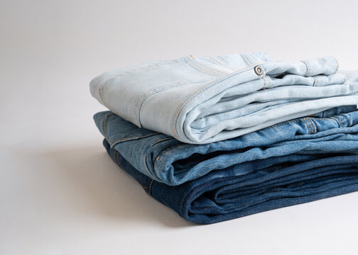 A neat stack of folded denim jeans in varying shades of blue against a clean white background.