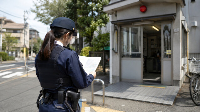 A Metropolitan Police Station Guard Post Security Duty Photograph of a Female Police Officer in Full Uniform Reviewing a Paper Navigation Map Outside a Local Koban Facility