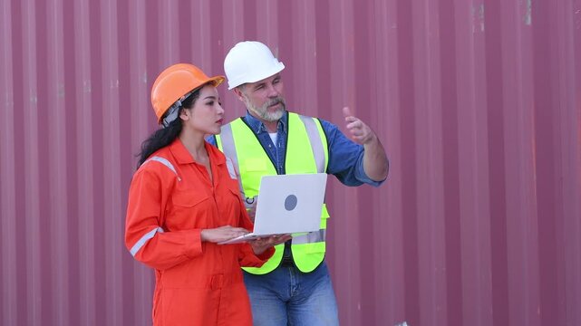 Engineers wearing safety helmets and high visibility clothing discussing logistics and inspecting shipping terminal representing container management freight.