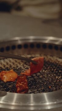 Close-up of raw A5 Wagyu beef slice held with tongs over Charcoal Grill, Japanese Yakiniku concept, 4K Vertical Video