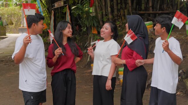 A group of Indonesian people are holding their country flag while smiling and talking to each other. Indonesia Independence Day concept.