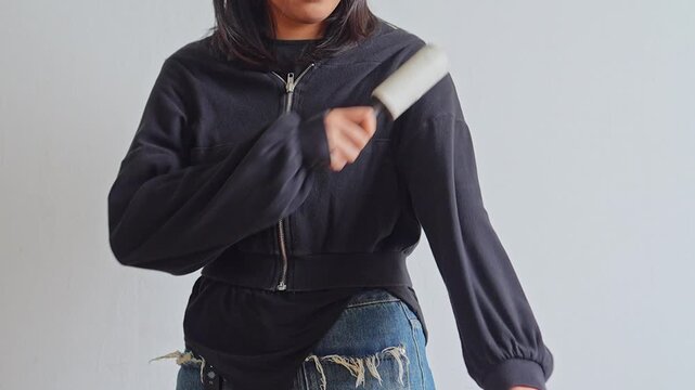 Person zipping up black sweater and rolling lint remover across sleeves for clothing maintenance