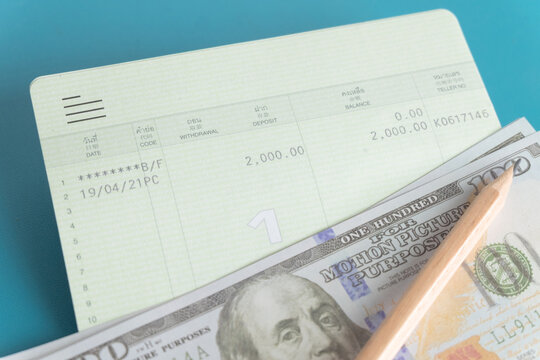 Close up of a bank savings passbook, US dollar bills and a wooden pencil on a blue background. Concept of personal finance, saving money, daily budgeting, wealth management and financial planning.