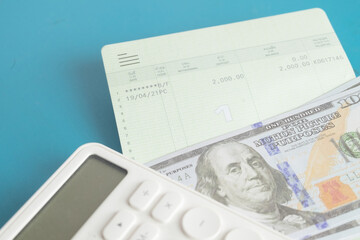 Obraz premium Close up of a white calculator, bank savings passbook and US dollar bills on a blue background. Concept of personal finance, saving money, budget calculation, accounting and wealth management.
