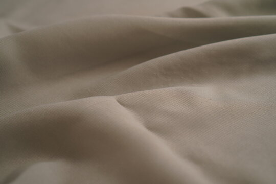 Soft gray fabric drapes elegantly with gentle folds. Light catches subtle texture and natural creases. Minimalist tone suits modern fashion or interior design. Perfect for backgrounds