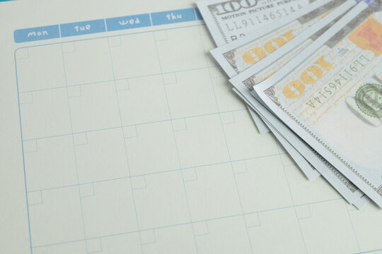 Close up of US dollar bills on a blank calendar planner with copy space. Concept of financial planning, monthly budgeting, payday schedule, tax deadline, loan payment date and saving strategy.